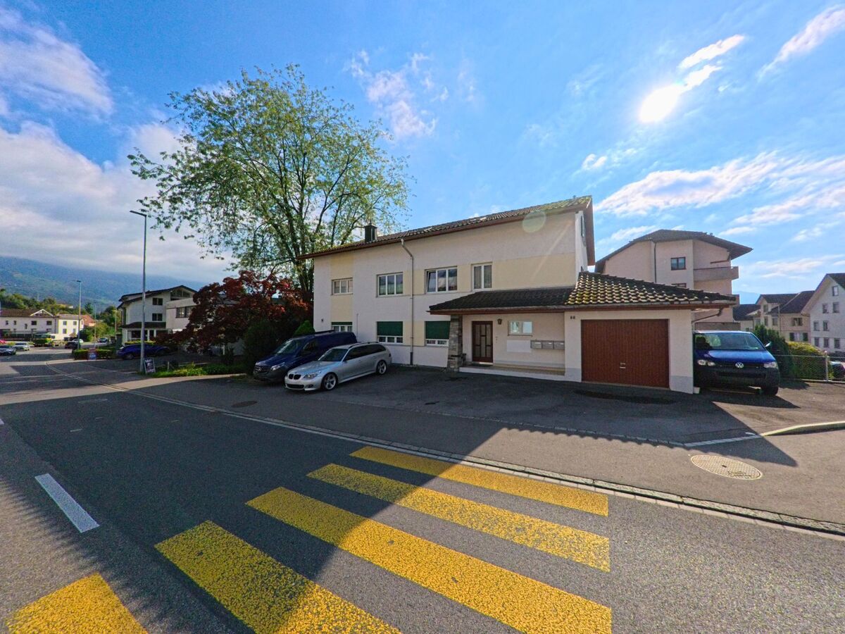 Ein Wohnhaus mit Garage in Kaltbrunn (8722, Kanton St. Gallen) liegt an einer Strasse mit Zebrastreifen, umgeben von weiteren Hausern und vereinzelten Fahrzeugen.