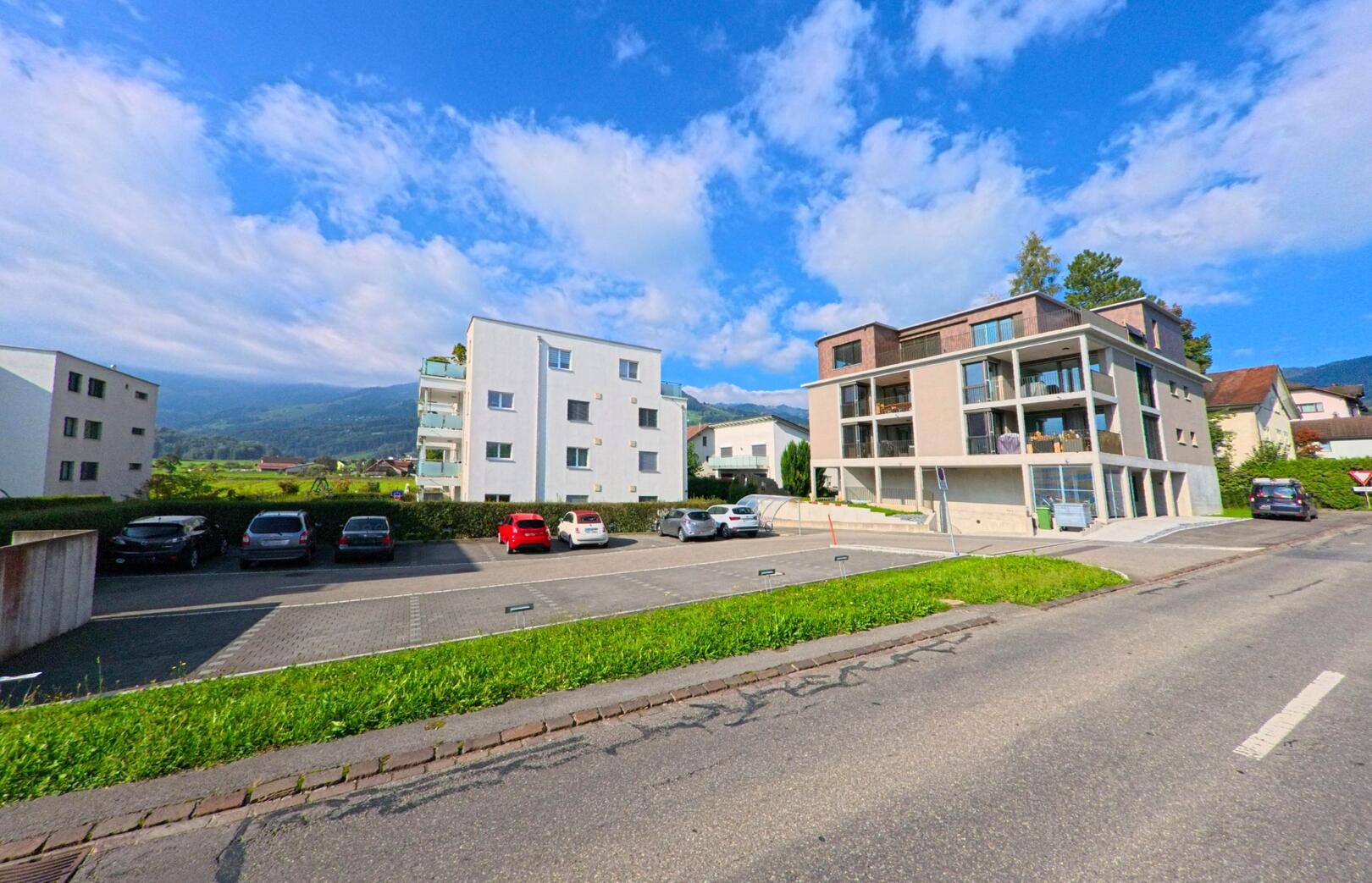 Vor moderner Wohnbebauung in Kaltbrunn (8722, Kanton St. Gallen) erstreckt sich ein Parkplatz mit Blick auf die umliegenden Hügel.