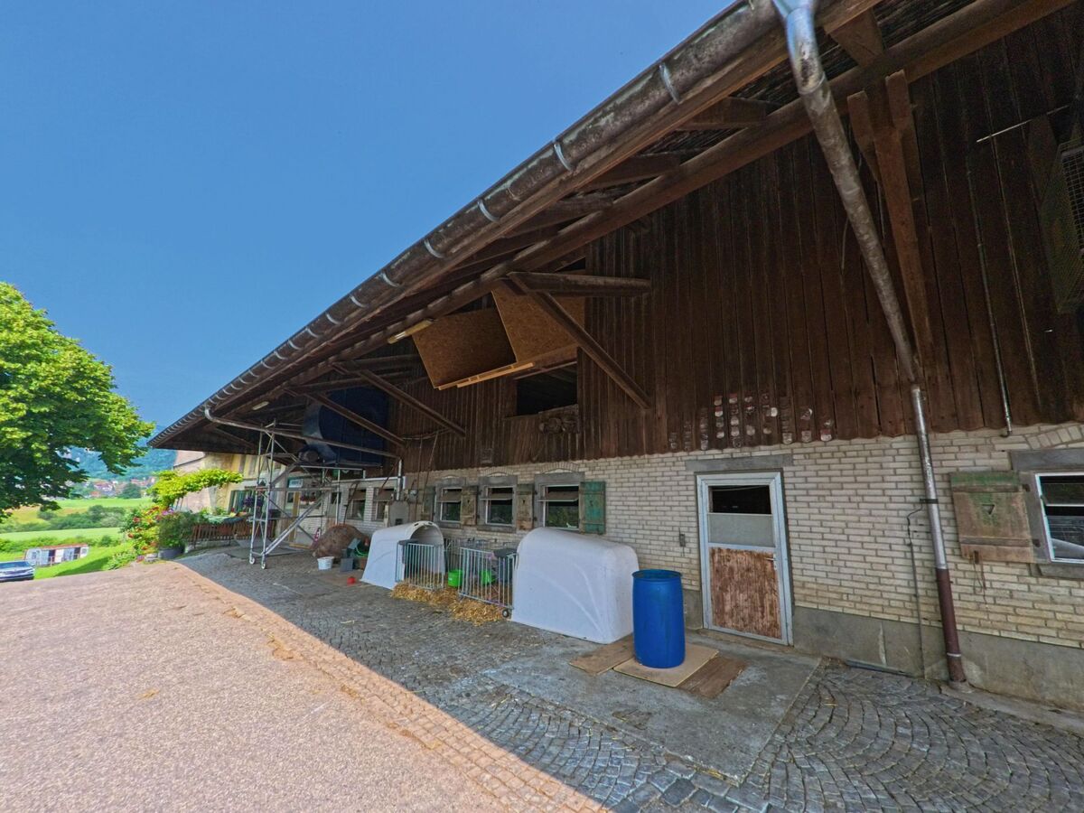 An einem Bauernhof in Kammersrohr (4535, Kanton Solothurn) sind Stallungen mit kleinen Gehegen und landwirtschaftlichem Material zu sehen.