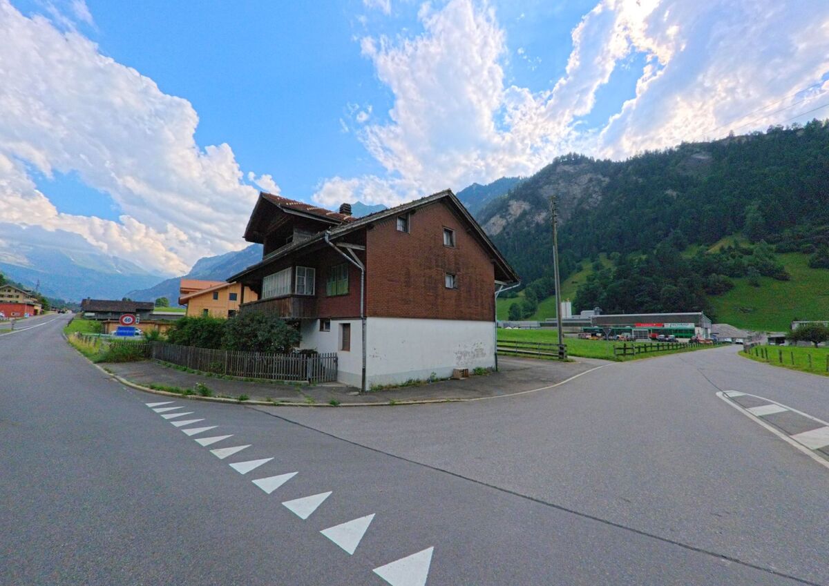In Kandergrund (3716, Kanton Bern) steht ein freistehendes Haus an einer dreifach verzweigten Kreuzung, umgeben von weitläufigem Tal und Berghängen im Hintergrund.