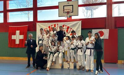 Kinder und Jugendliche stehen in Karateanzuegen mit Medaillen auf einem Podest in einer Turnhalle in Grenchen (2540, Kanton Solothurn).