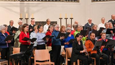 In Dübendorf (8600, Kanton Zürich) singt der katholische Kirchenchor Cäcilia mit Notenmappen in einem Kirchenraum, begleitet von Instrumenten.