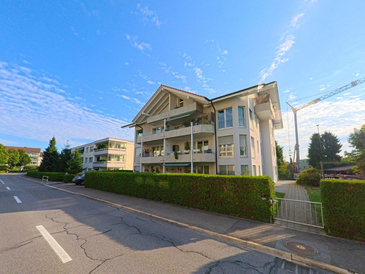 Ein modernes Mehrfamilienhaus mit Balkonen steht in Kehrsatz (3122, Kanton Bern) an einer ruhigen Strasse mit gepflegten Hecken.