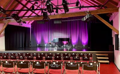 Eine kleine Theaterbuehne mit Fluegel und Beleuchtung ist vor Sitzreihen in Murten (3280, Kanton Freiburg) aufgebaut.