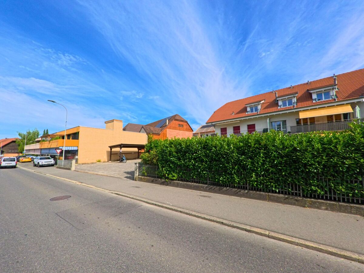 In einem Wohnquartier von Kerzers (3207, Kanton Freiburg) stehen moderne Reihenhäuser mit roten Dächern und gelber Markise entlang einer ruhigen Strasse.