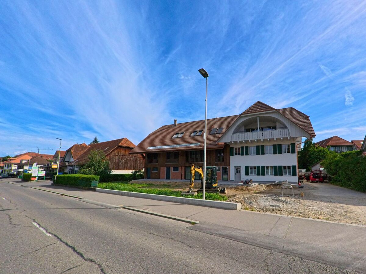 An einer Hauptstrasse in Kerzers (3207, Kanton Freiburg) wird der Vorplatz eines grossen Wohnhauses mit Holz- und Putzfassade gerade neu gestaltet.