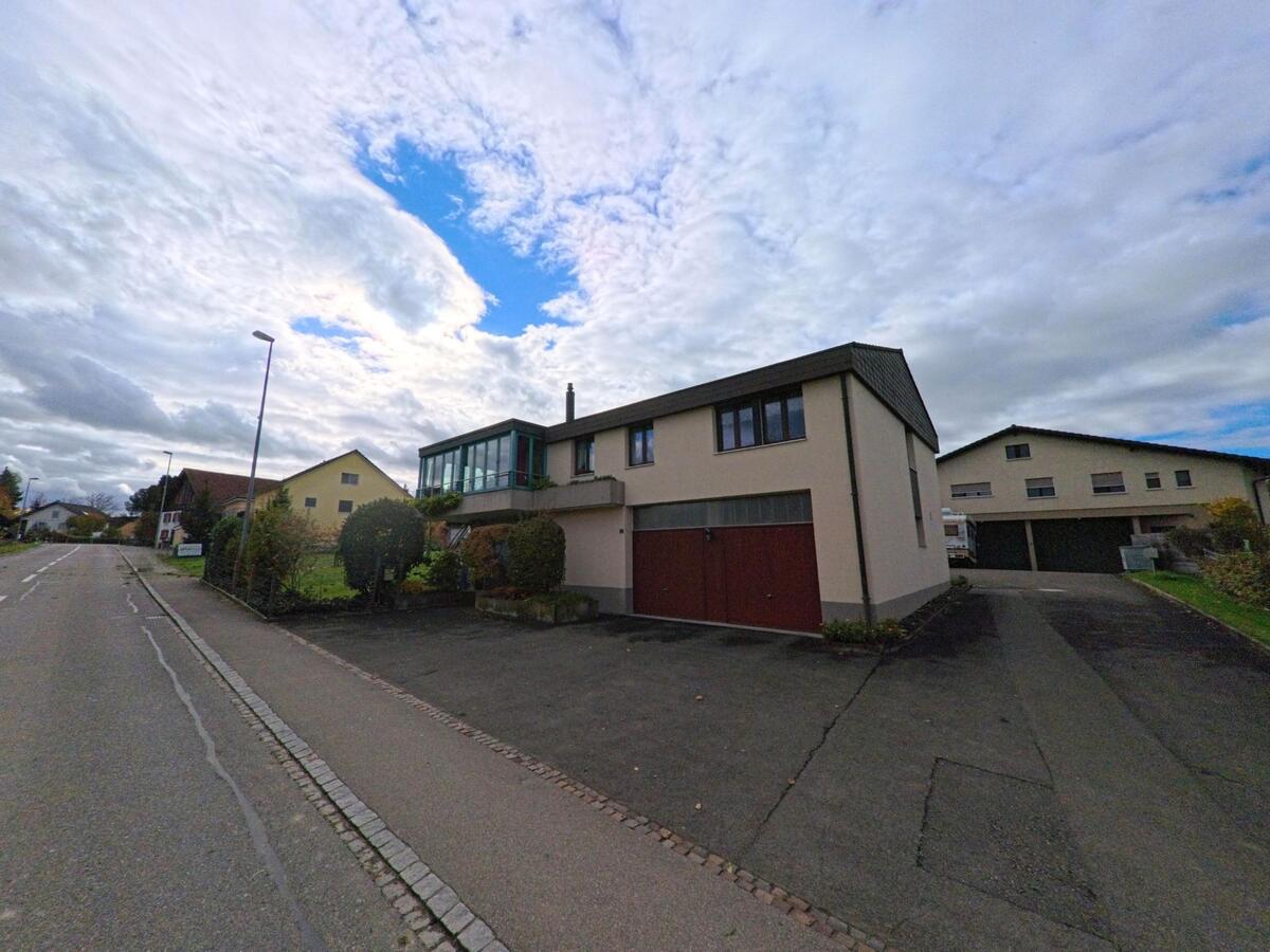 Ein niedriges Gebäude mit grossen Garagentoren und einem verglasten Anbau steht in Kesswil (8593, Kanton Thurgau) an einer ruhigen Strasse unter einem wolkenreichen Himmel.