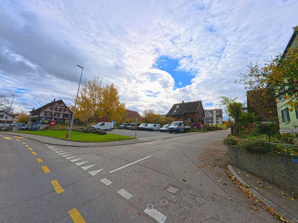 An einer Kreuzung in Kesswil (8593, Kanton Thurgau) liegt ein Parkplatz mit Lieferwagen neben einer Grünfläche, während ein markantes Fachwerkhaus und herbstliche Bäume das Ortsbild prägen.