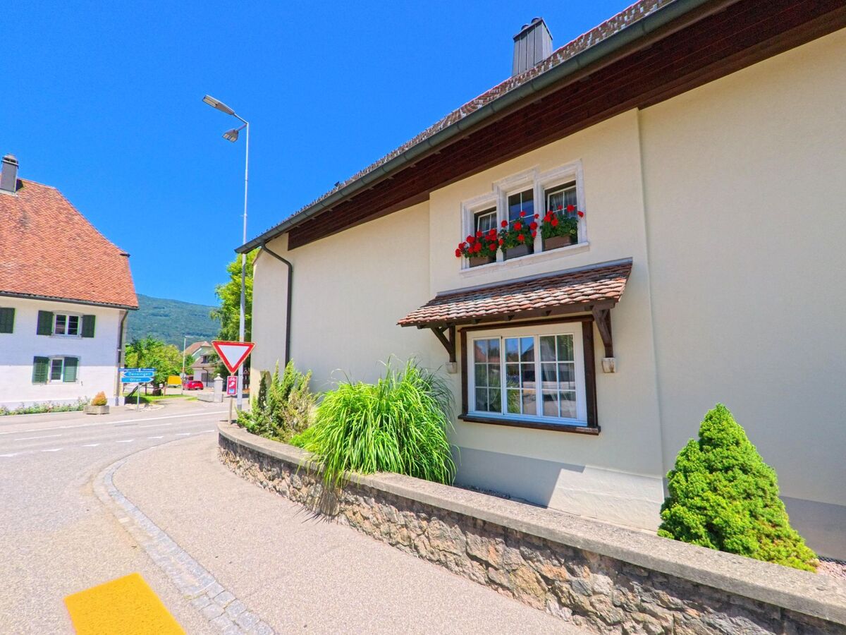 In Kestenholz (4703, Kanton Solothurn) steht an einer Strassenecke ein gepflegtes Haus mit Blumenschmuck und Vorgarten, eingerahmt von einer niedrigen Natursteinmauer.