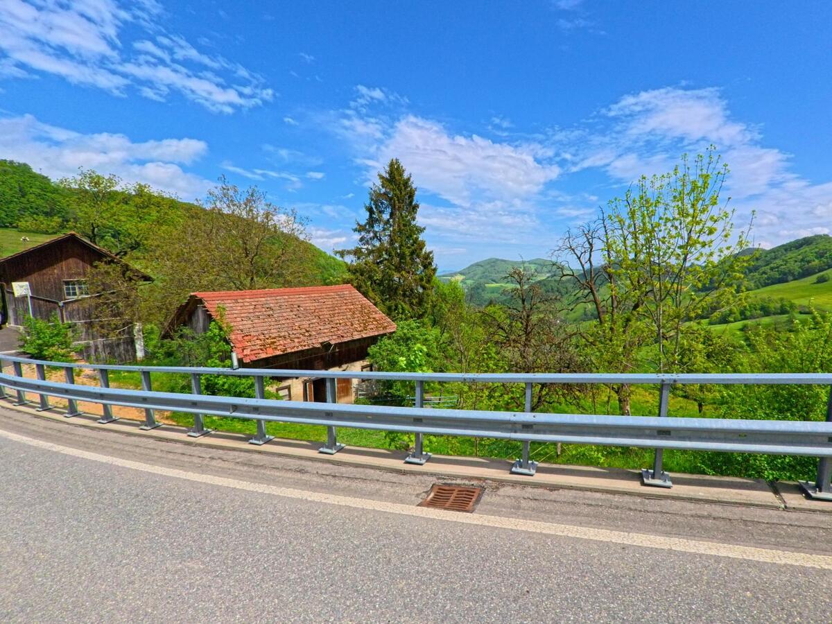 In Kienberg (4468, Kanton Solothurn) stehen zwei kleine Holzgebäude oberhalb eines Abhangs mit weiter Sicht auf bewaldete Hügel und Wiesen.