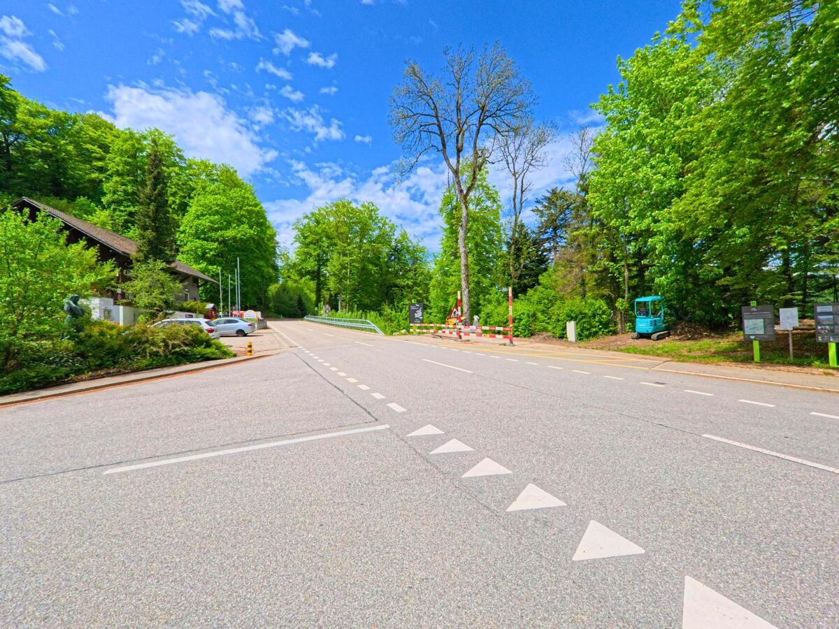An einem Waldrand in Kienberg (4468, Kanton Solothurn) führt eine breite Strasse mit Baustellenabsperrung vorbei an einem Parkplatz und Infotafeln.