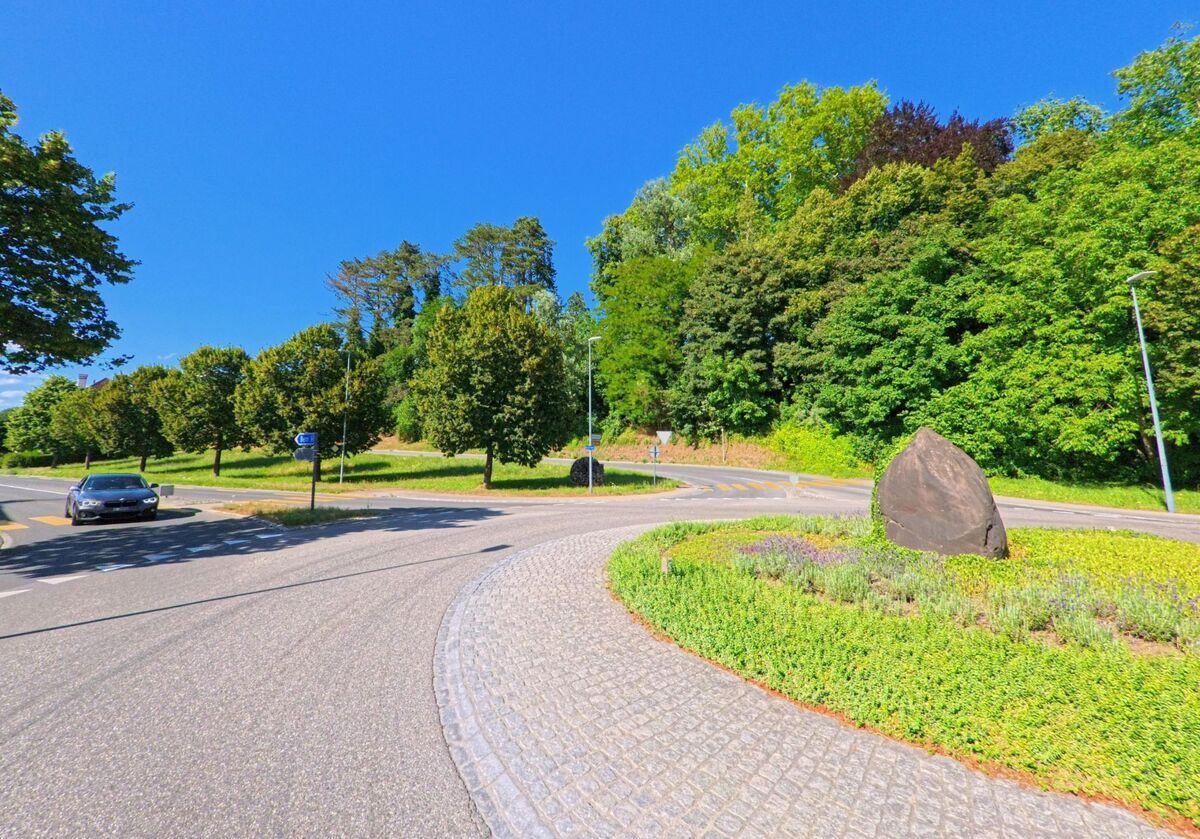 In Kiesen (3629, Kanton Bern) markiert ein bepflanzter Kreisel mit einem grossen Naturstein den Übergang von einer Allee in eine bewaldete Hügellandschaft.