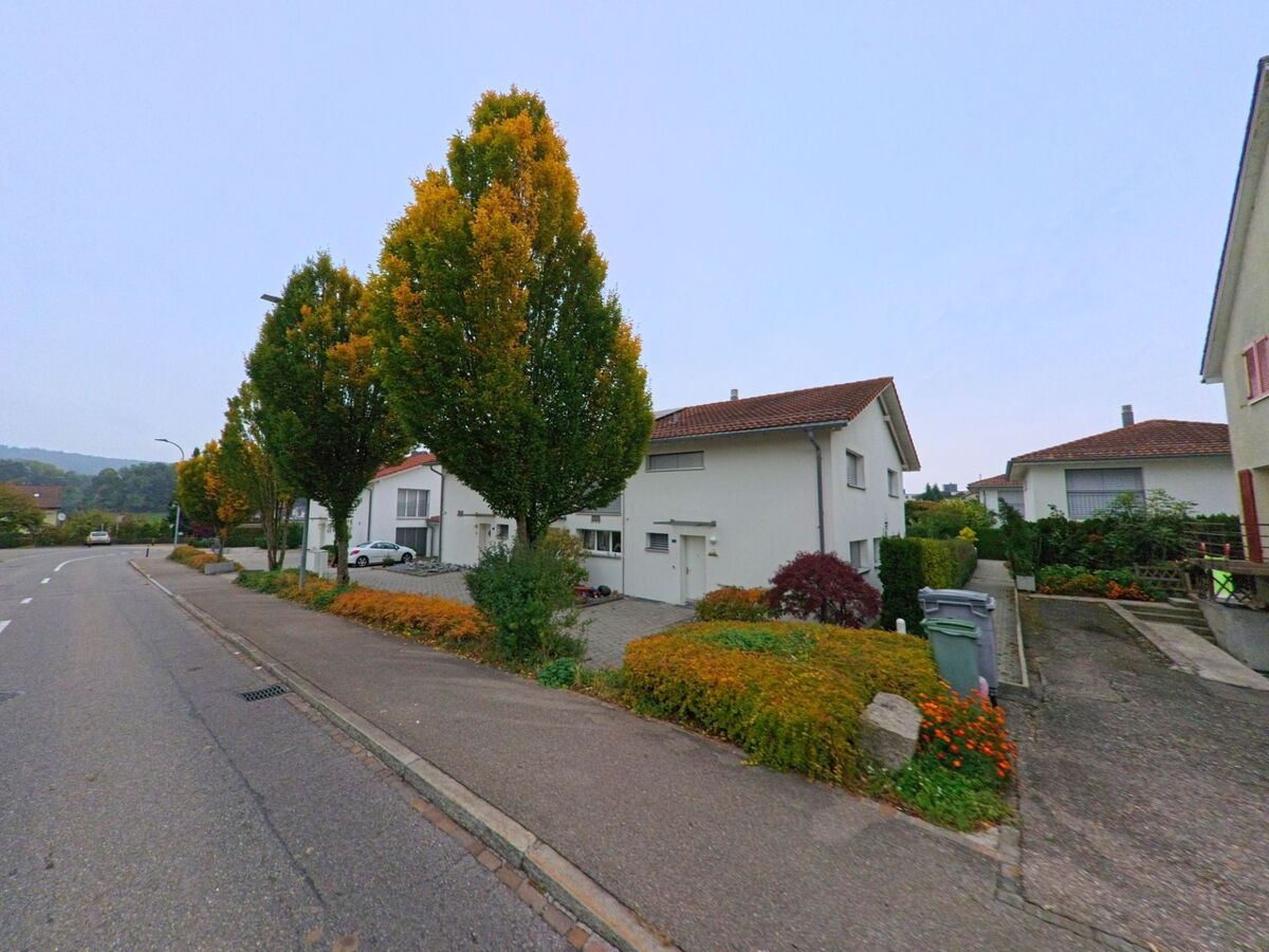Entlang einer Wohnstrasse in Killwangen (8956, Kanton Aargau) stehen Einfamilienhäuser mit gepflegten Vorgärten und herbstlich gefärbten Bäumen.