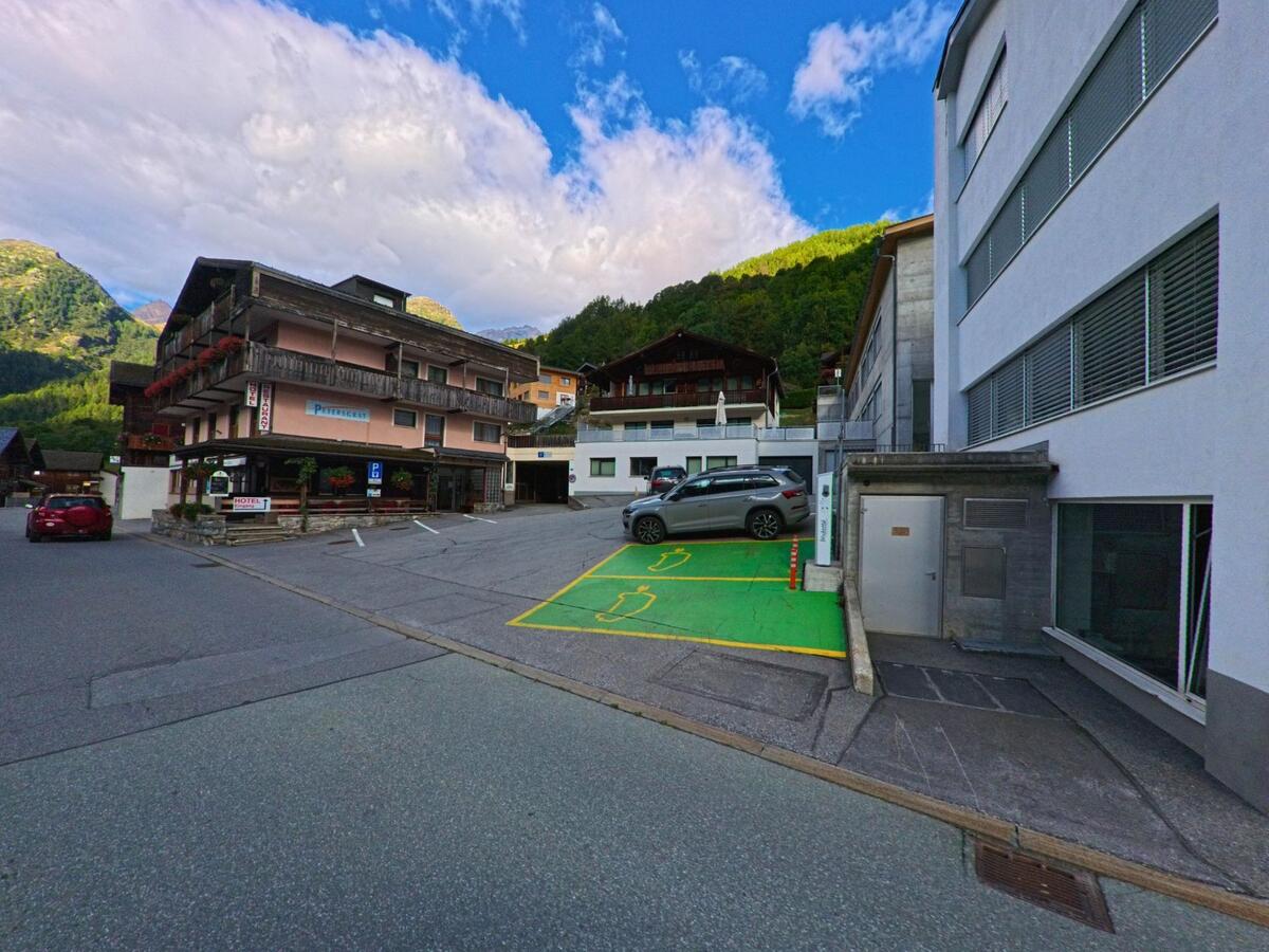 Im Zentrum von Kippel (3917, Kanton Wallis) steht ein Hotel mit Balkonen, daneben befinden sich moderne Gebaeude und ein Parkplatz mit markierten Stellflaechen.