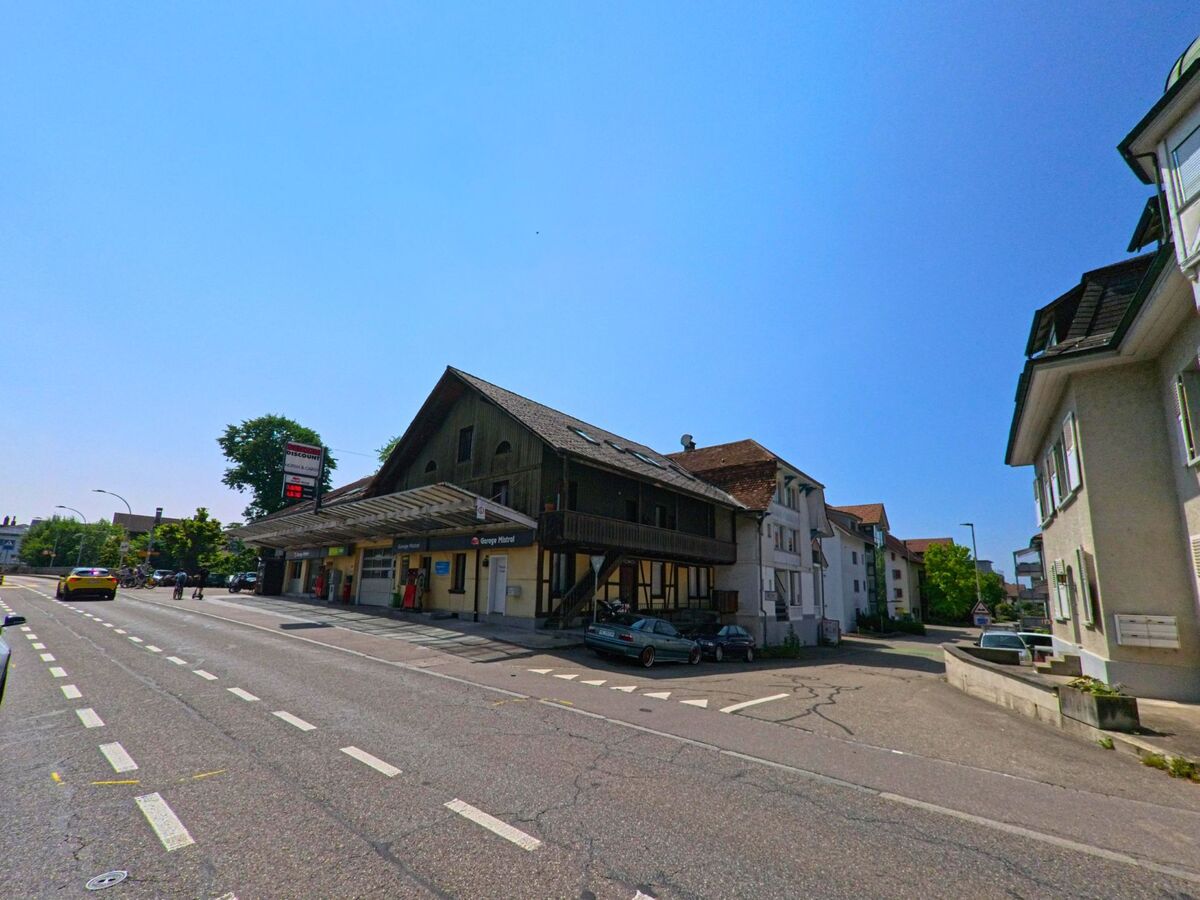 In Kirchberg (3422, Kanton Bern) steht ein rustikales Bahnhofsgebäude mit Holzfassade und Vordach an einer belebten Hauptstrasse.