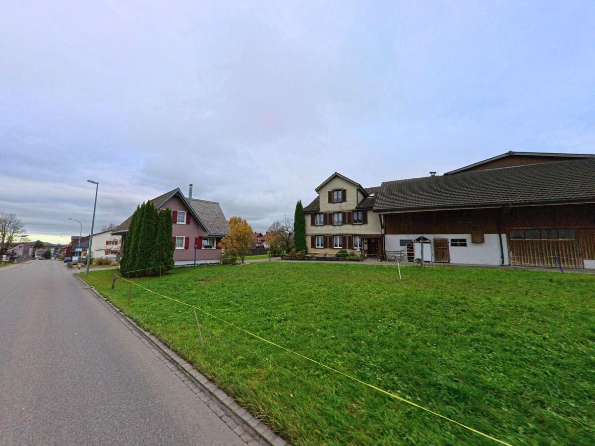 In Kirchberg (9602, Kanton St. Gallen) grenzen ein traditionelles Wohnhaus und ein grosser Hof direkt an eine weite Gruenflaeche entlang einer ruhigen Strasse.