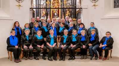 Eine Chorgruppe in schwarzer Kleidung und blauen Schals posiert vor dem reich verzierten Altar einer Kirche in Sursee (6210, Kanton Luzern).