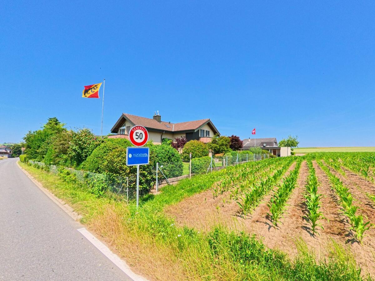In Kirchlindach (3038, Kanton Bern) ist die Straße von einem Feld mit frisch gepflanztem Mais gesäumt, und ein Ortsschild für Oberlindach zeigt den Beginn des Gebiets.