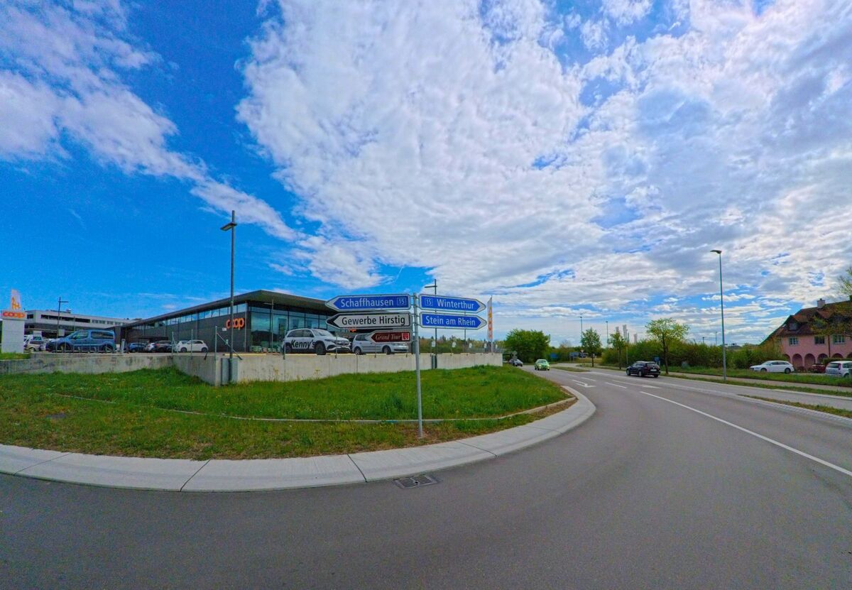 Am Rand von Kleinandelfingen im Kanton Zürich (PLZ 8451) befindet sich ein modernes Einkaufszentrum mit Coop-Filiale, an dem mehrere Wegweiser in Richtung Schaffhausen, Winterthur und Stein am Rhein zeigen.