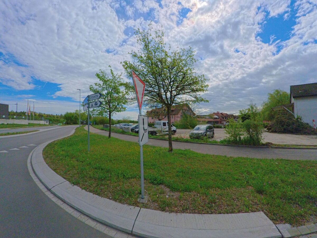 Am Ortseingang von Kleinandelfingen im Kanton Zürich (PLZ 8451) weist ein Verkehrsschild auf die Richtung zum Ortszentrum hin, während sich im Hintergrund ein Parkplatz und Wohnhäuser befinden.