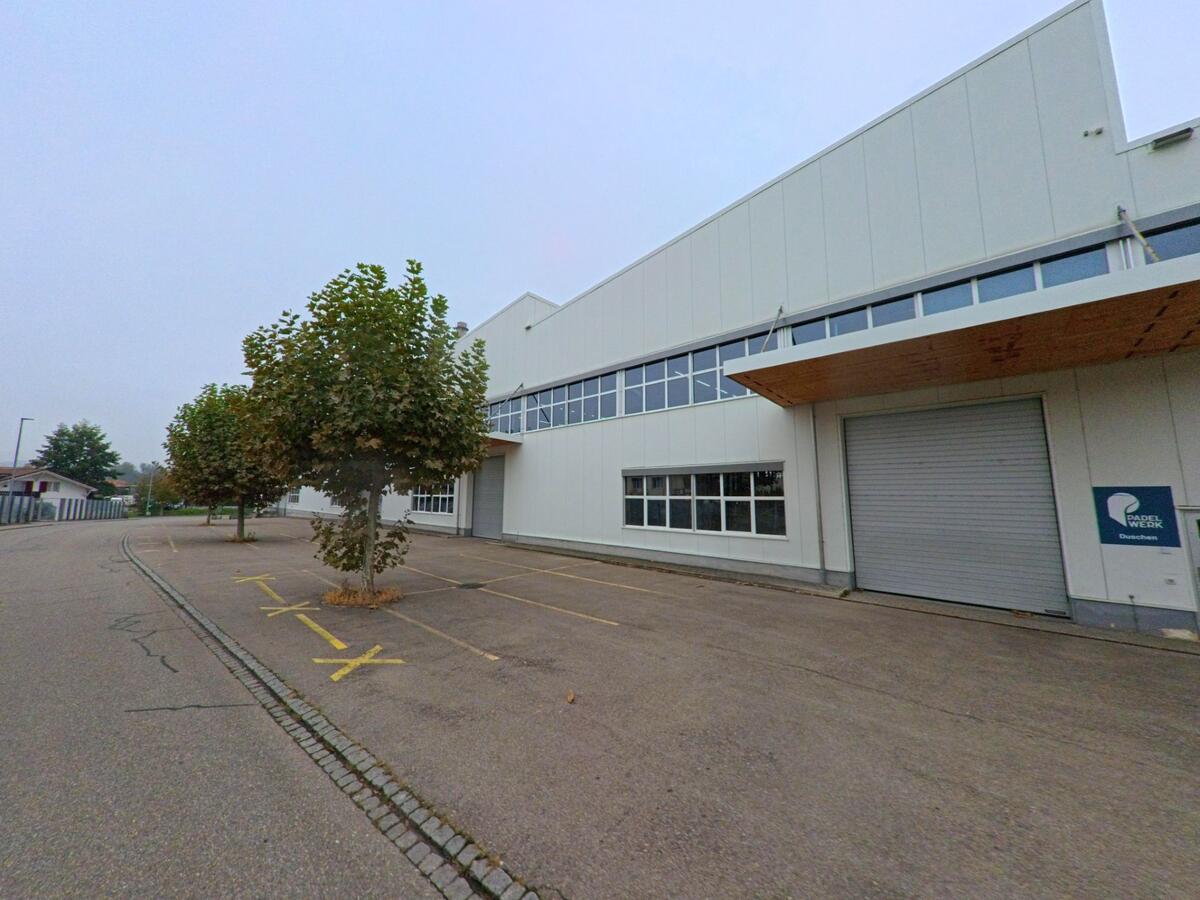 Ein modernes Industriegebäude in Klingnau (5313, Kanton Aargau) mit Rolltor und Parkplätzen liegt an einer ruhigen Strasse mit Bäumen am Rand.