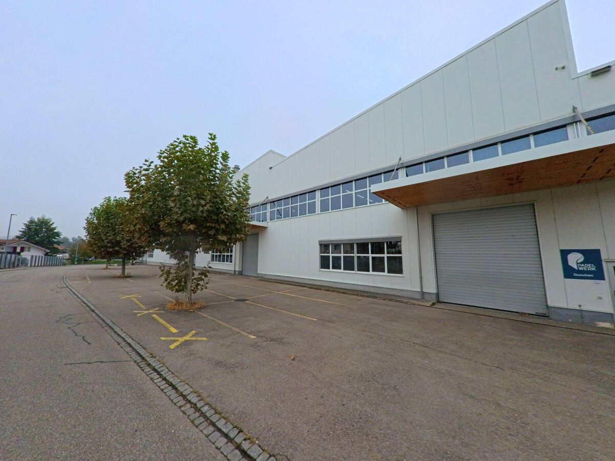 Ein modernes Industriegebäude in Klingnau (5313, Kanton Aargau) mit Rolltor und Parkplätzen liegt an einer ruhigen Strasse mit Bäumen am Rand.