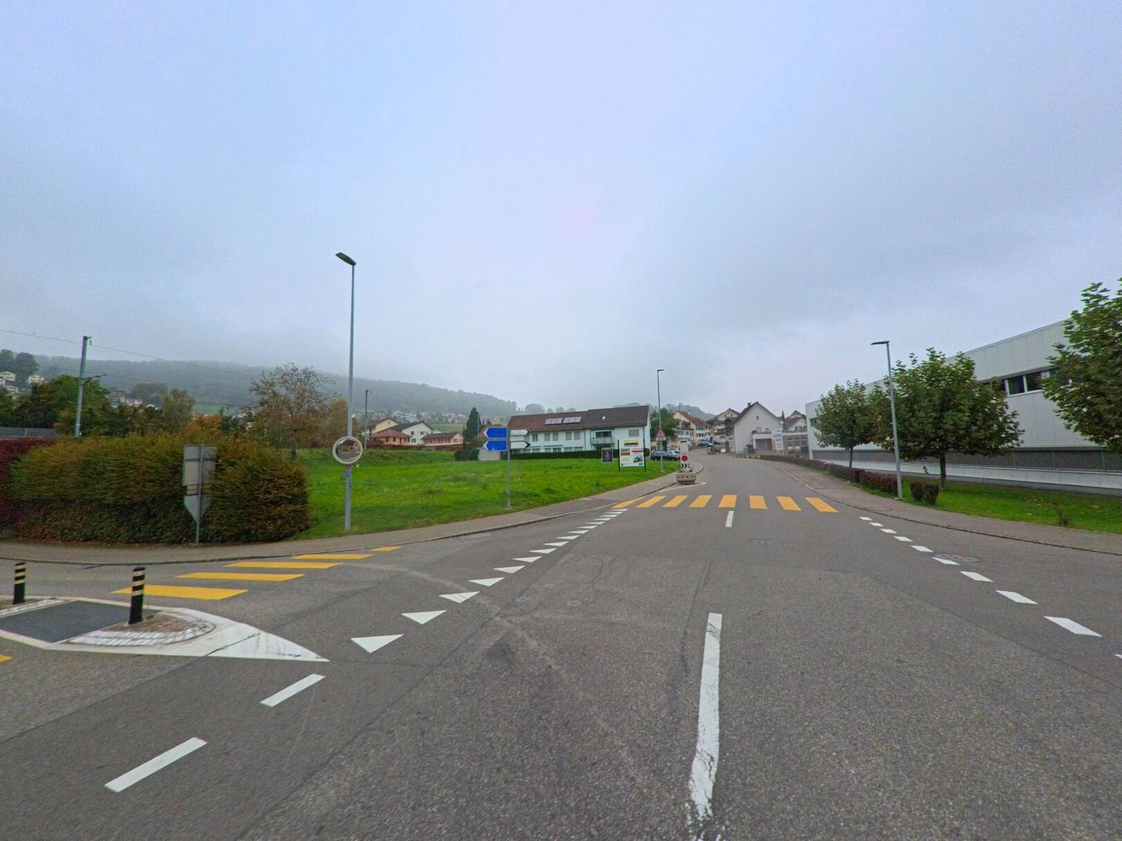In Klingnau (5313, Kanton Aargau) führt eine breite Strasse mit markiertem Fussgängerstreifen vorbei an Wohnhäusern und modernen Gebäuden in Richtung Ortszentrum.