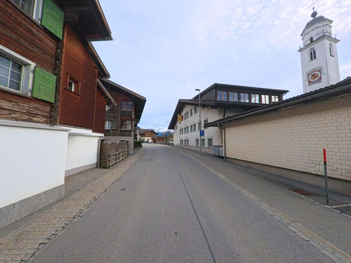 Eine leicht geschwungene Strasse mit Wohnhäusern und Blick auf den Kirchturm prägt das Ortsbild von Klosters (7247, Kanton Graubünden).