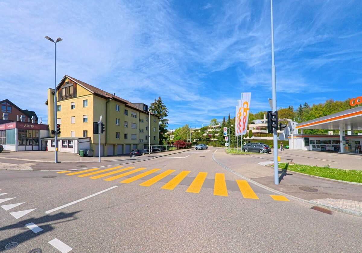 In Kloten, PLZ 8302 im Kanton Zürich, treffen sich eine Coop-Tankstelle, Wohnhäuser und ein Zebrastreifen an einer belebten Kreuzung mit Ampelanlage.