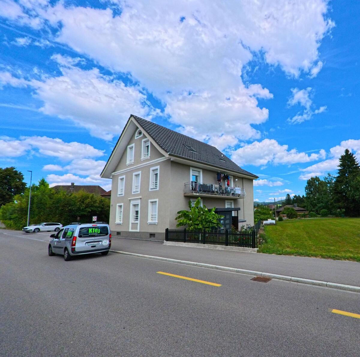 Ein freistehendes Mehrfamilienhaus mit Balkon und angrenzender Wiese steht in Kölliken (5742, Kanton Aargau) an einer ruhigen Wohnstrasse.