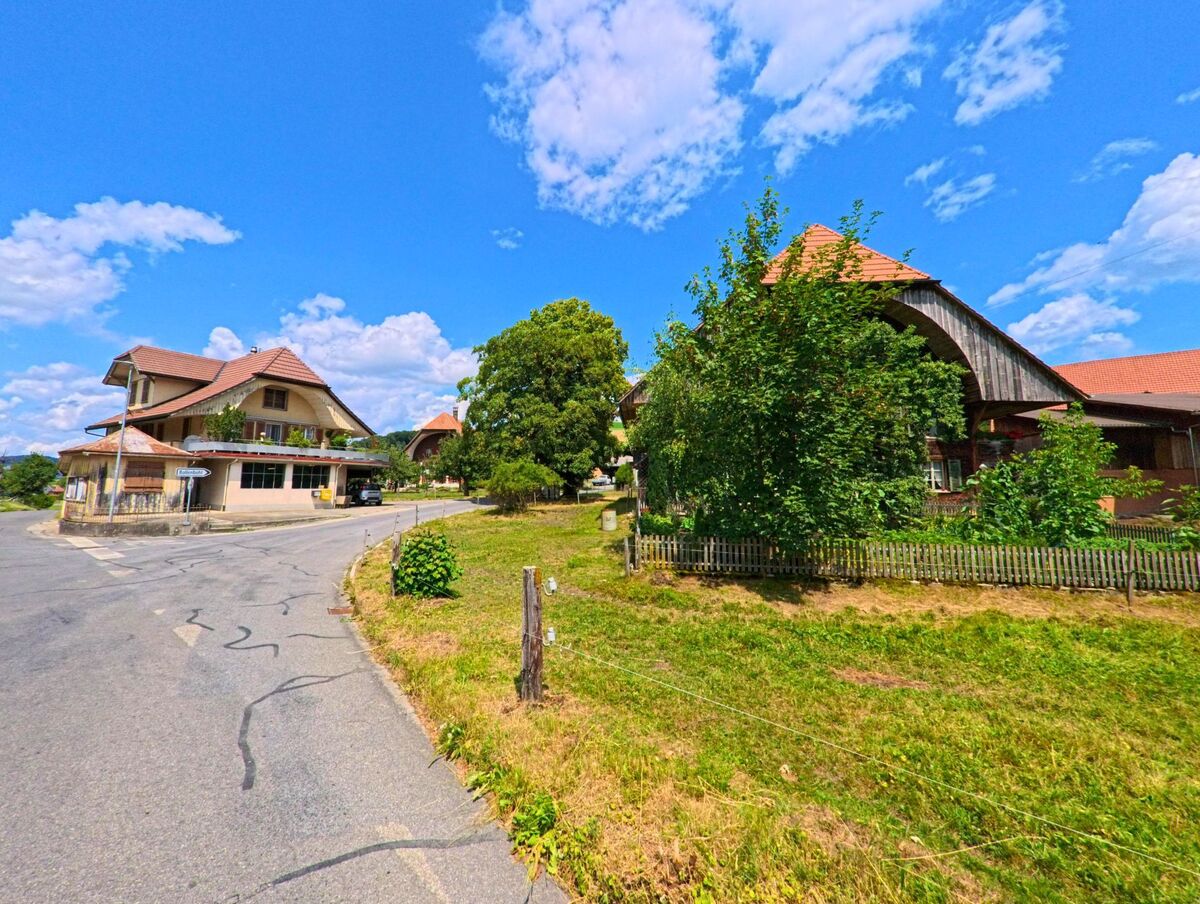 In Konolfingen (PLZ 3503, Kanton Bern) liegen traditionelle Wohn- und Bauernhäuser mit gepflegten Vorgärten entlang einer sanft geschwungenen Dorfstrasse.