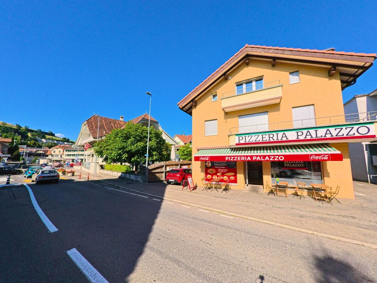 An der Hauptstrasse von Konolfingen (PLZ 3503, Kanton Bern) befindet sich die Pizzeria Palazzo mit Aussensitzplätzen vor einem gelben Wohn- und Geschäftshaus.