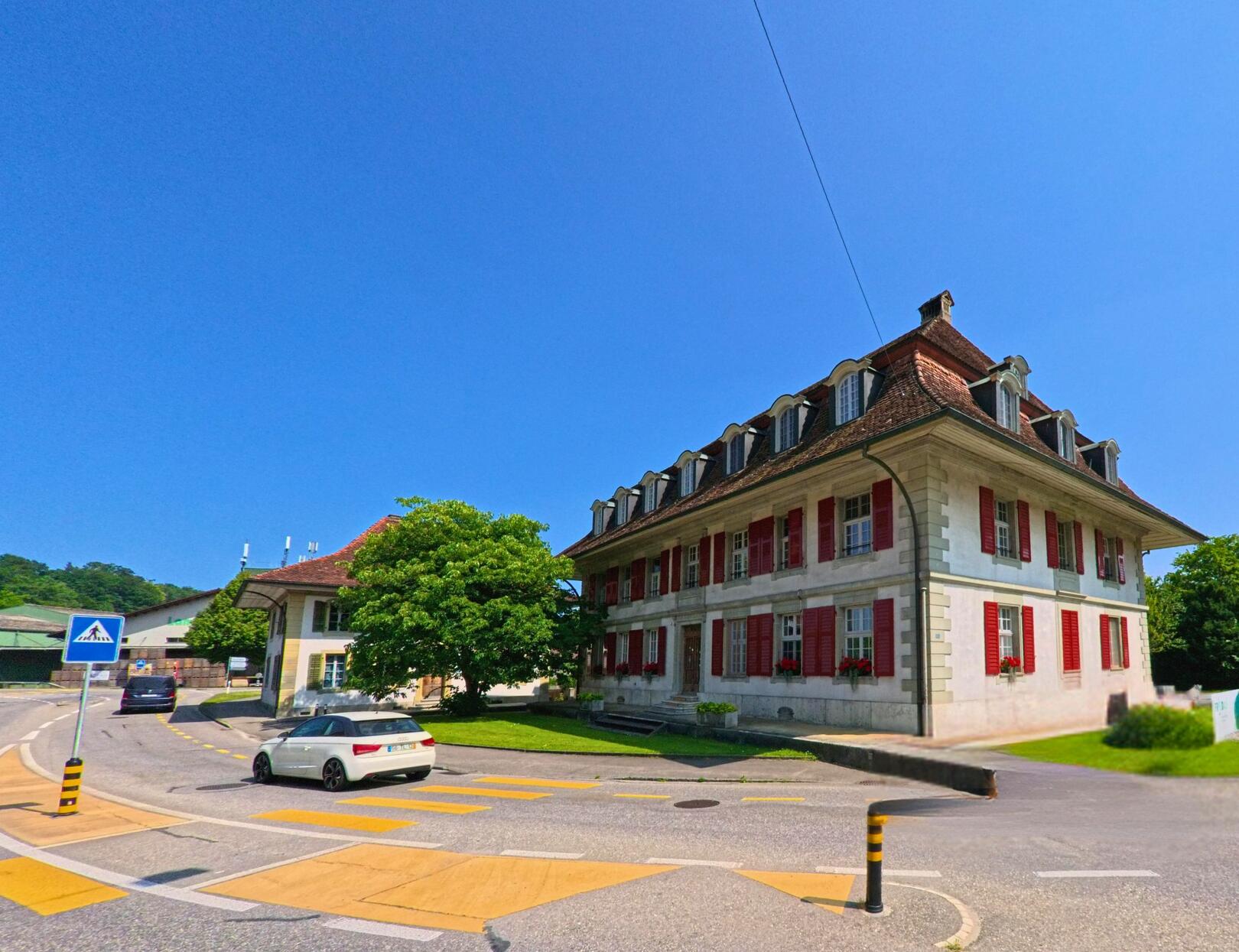 In Koppigen (3425, Kanton Bern) steht an einer verkehrsberuhigten Kreuzung ein markantes Gebäude mit roten Fensterläden und Mansarddach aus der Zeit des Barock.