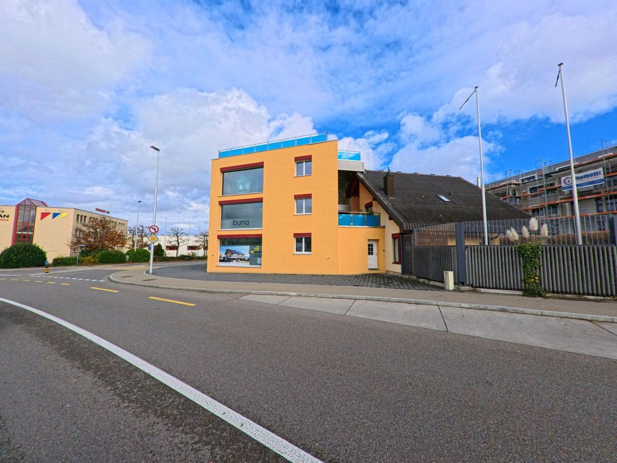 Ein modernes, orangefarbenes Gebäude mit grossen Fenstern steht in Kreuzlingen (8280, Kanton Thurgau) an einer breiten Strasse unter wolkigem Himmel.