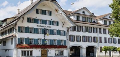 Das Gasthaus zur Krone in Escholzmatt (6182, Kanton Luzern) ist ein traditionelles Gebäude mit grünen Fensterläden, Blumenschmuck und historischer Fassade.