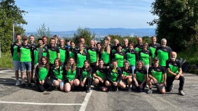 Gruppenfoto des KTV Einsiedeln mit Mitgliedern in grün-schwarzer Vereinskleidung vor hügeliger Landschaft, aufgenommen in Einsiedeln (8840, Kanton Schwyz).