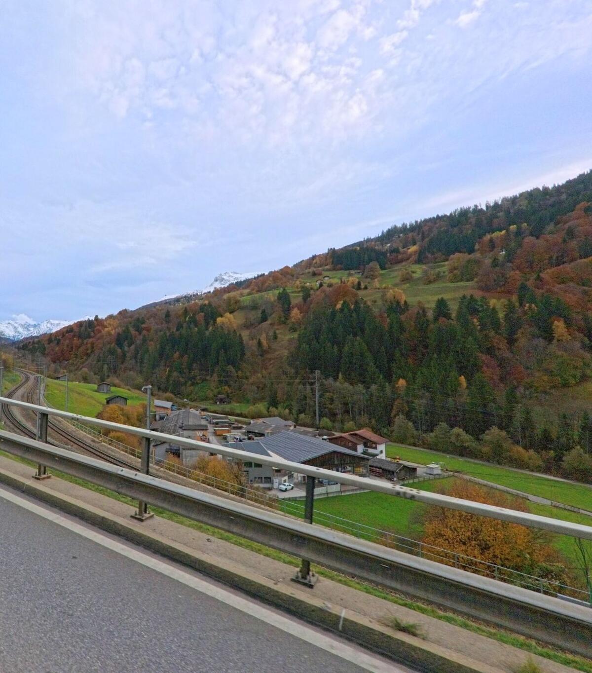 Von einer Brücke aus fällt der Blick auf Bahnlinien, Gewerbebauten und bewaldete Hänge im Tal von Küblis (7240, Kanton Graubünden) bei ruhiger Herbststimmung.
