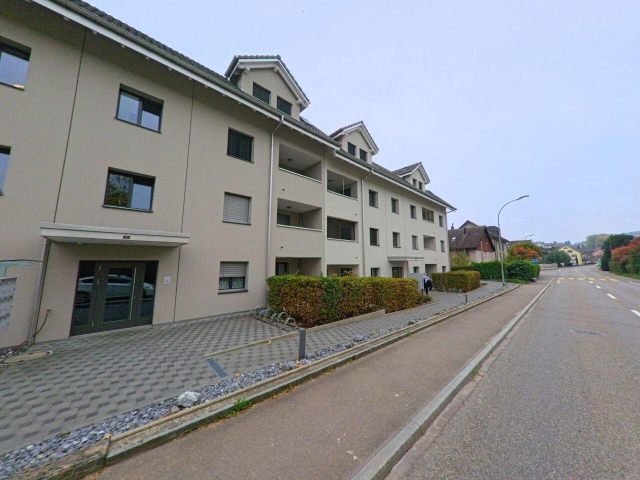 Ein modernes Mehrfamilienhaus in Künten (5444, Kanton Aargau) steht an einer ruhigen Strasse mit breitem Trottoir und gepflegten Hecken.