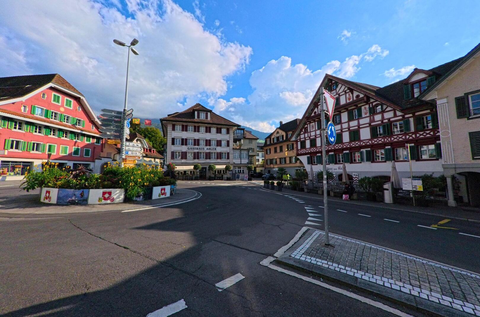 Zwischen traditionellen Fassaden in Kuessnacht (6403, Kanton Schwyz) fuehrt eine kurvige Strasse an einem bunt bepflanzten Kreisverkehr vorbei.