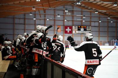 Eishockeyspieler des Küssnachter Schlittschuh Clubs stehen an der Bande einer Eishalle und klatschen sich während eines Spiels ab, in Küssnacht, 6403, Kanton Schwyz.