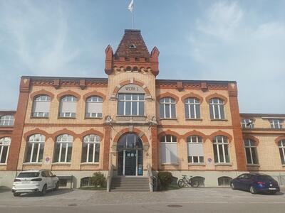 Die symmetrische Backsteinfassade eines historischen Gebaeudes mit zentralem Eingang praegt diese Strassenansicht in Gossau (9200, Kanton St. Gallen) unter hellem Himmel.