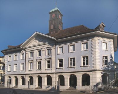 Das Kunsthaus Langenthal in Langenthal (4900, Kanton Bern) zeigt sich in klassizistischer Architektur mit heller Fassade und Uhrturm unter blauem Himmel.