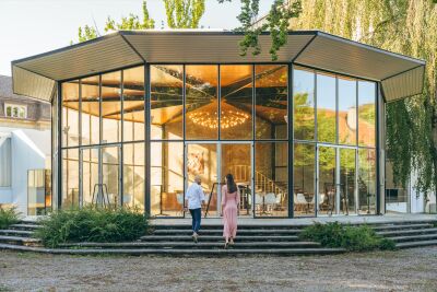 Vor dem Kurtheater in Baden (5400, Kanton Aargau) gehen zwei Personen eine Treppe hinauf, während das warme Licht durch die Glasfront fällt.