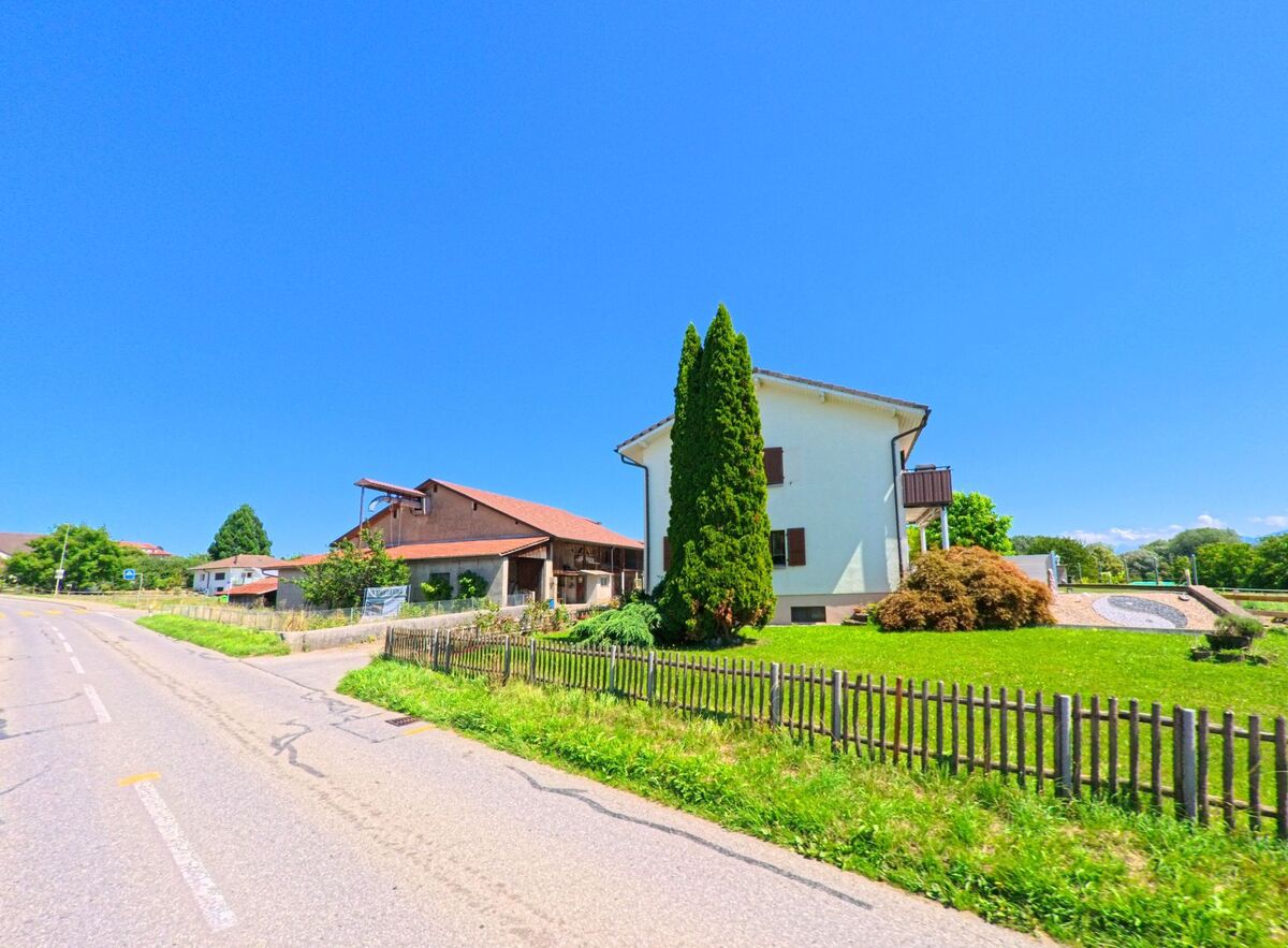 An einer Strasse in La Brillaz (1745, Kanton Freiburg) steht ein Wohnhaus mit angrenzendem Garten, vor dem eine grosse bepflanzte Sonnenuhr angelegt ist.