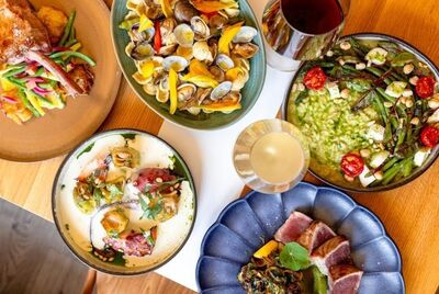 Im Restaurant La Charrue in Aclens (1123, Kanton Waadt) sind mehrere Teller mit bunt angerichteten Speisen und Gläsern auf einem Holztisch serviert.