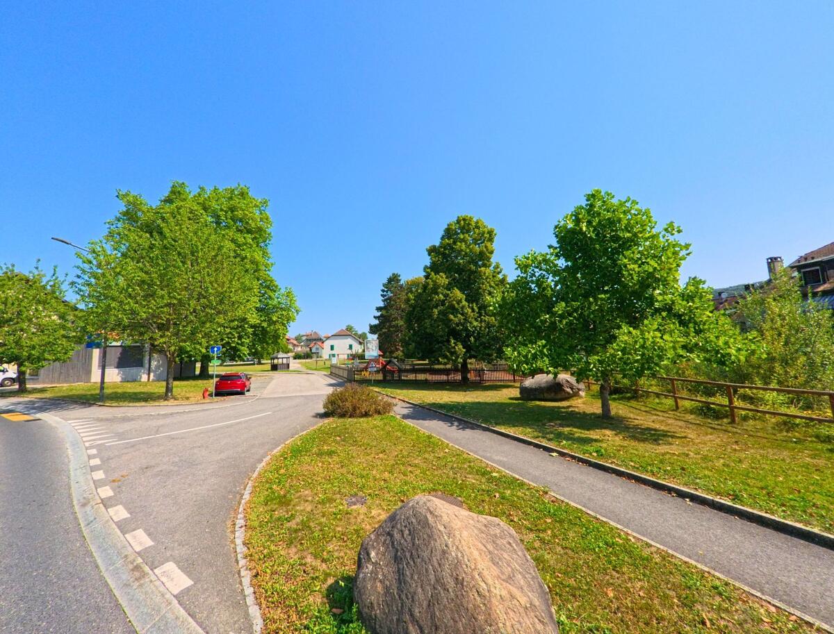 Ein kleiner Park mit Baeumen und einem Fussweg liegt in La Chaux (Cossonay, 1308, Kanton Waadt) direkt neben der Strasse am Dorfeingang.