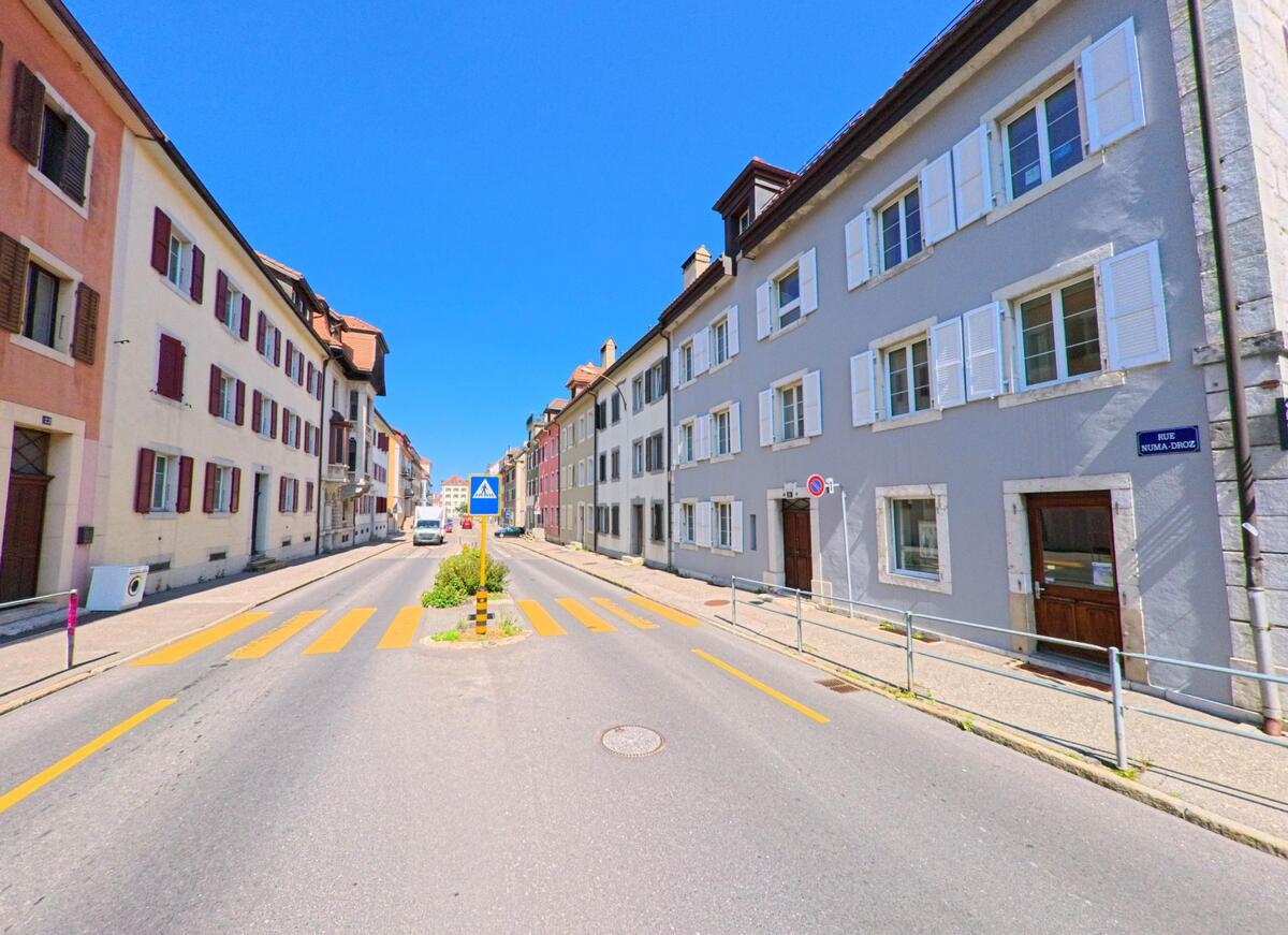 Eine gerade Strasse in La Chaux-de-Fonds (2300, Kanton Neuenburg) ist gesaeumt von mehrgeschossigen Wohnhaeusern mit Fensterlaeden und einem Fussgaengerueberweg.