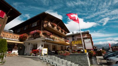 In Sedrun (7188, Kanton Graubuenden) befindet sich La Conditoria, ein traditionelles Cafe-Gebaeude mit Holzfassade, Blumenschmuck und Schweizer Flagge.