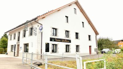 Das Restaurant La Cuisine de l’Apothicaire in Bonfol (2944, Kanton Jura) befindet sich in einem hellen, traditionellen Gebäude mit steinernen Fensterrahmen.
