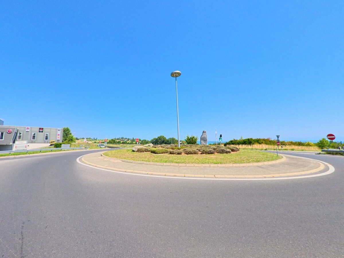 Ein Kreisverkehr in La Grande Beroche (2022, Kanton Neuenburg) ist von einer bepflanzten Mittelinsel mit Skulptur und Strassenlaterne gestaltet.